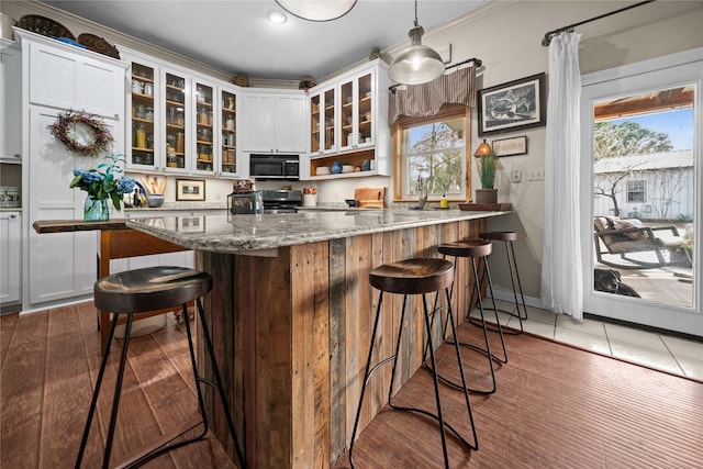 kitchen featuring white cabinetry, light wood-type flooring, a kitchen breakfast bar, pendant lighting, and light stone counters