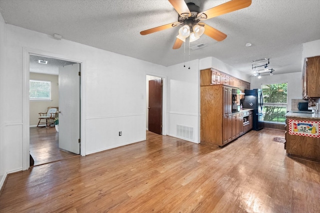 kitchen featuring ceiling fan, a textured ceiling, light hardwood / wood-style flooring, and black fridge