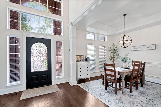 entrance foyer with dark wood-type flooring, an inviting chandelier, a raised ceiling, decorative columns, and a high ceiling