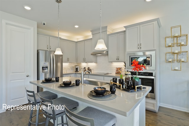 kitchen featuring a center island with sink, sink, hanging light fixtures, appliances with stainless steel finishes, and dark hardwood / wood-style flooring