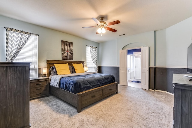 carpeted bedroom featuring ceiling fan, multiple windows, and ensuite bathroom