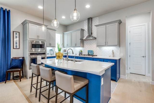 kitchen featuring sink, a breakfast bar area, appliances with stainless steel finishes, a center island with sink, and wall chimney exhaust hood