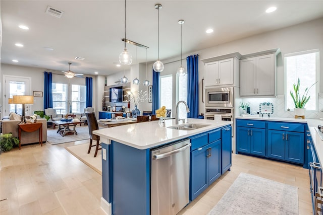 kitchen with blue cabinetry, sink, an island with sink, pendant lighting, and stainless steel appliances