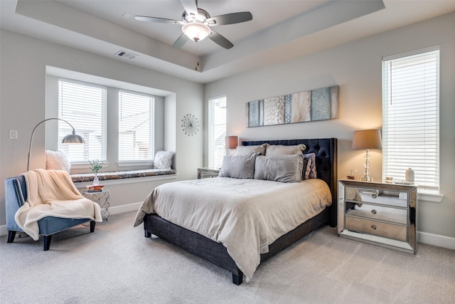 bedroom featuring light colored carpet, a raised ceiling, and ceiling fan