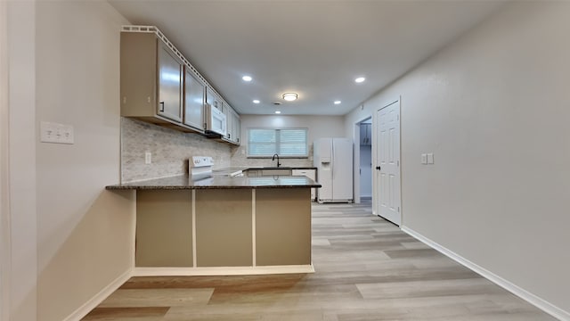 kitchen with white refrigerator with ice dispenser, dark stone counters, kitchen peninsula, range with electric stovetop, and light hardwood / wood-style flooring