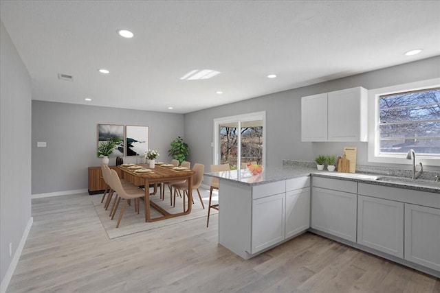 kitchen featuring light wood-style flooring, a sink, a peninsula, and light stone countertops