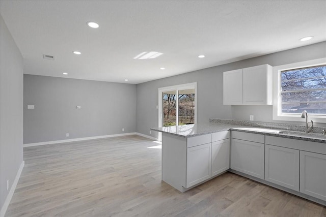 kitchen featuring white cabinetry, kitchen peninsula, light wood-type flooring, light stone counters, and sink