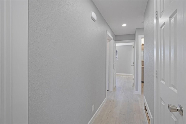 corridor with light wood-style flooring, baseboards, and a textured wall