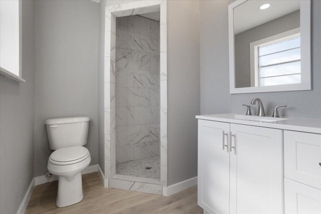 full bath with toilet, wood finished floors, vanity, baseboards, and tiled shower