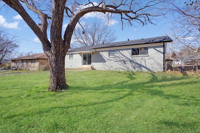 rear view of house with brick siding, a yard, and fence