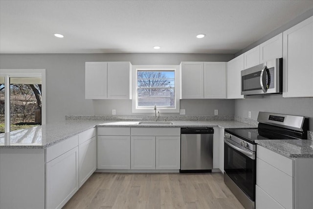 kitchen with light stone countertops, appliances with stainless steel finishes, white cabinetry, and light hardwood / wood-style flooring