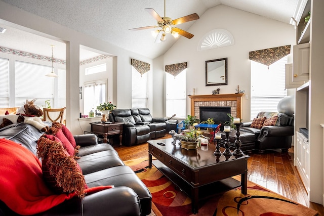 living room with ceiling fan, vaulted ceiling, a fireplace, hardwood / wood-style flooring, and a textured ceiling