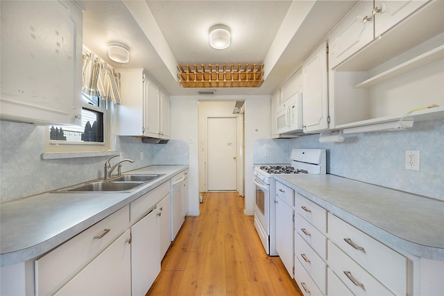 kitchen with sink, white appliances, white cabinetry, and light hardwood / wood-style floors