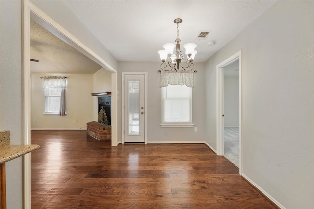 foyer entrance featuring a chandelier, wood finished floors, visible vents, baseboards, and a brick fireplace