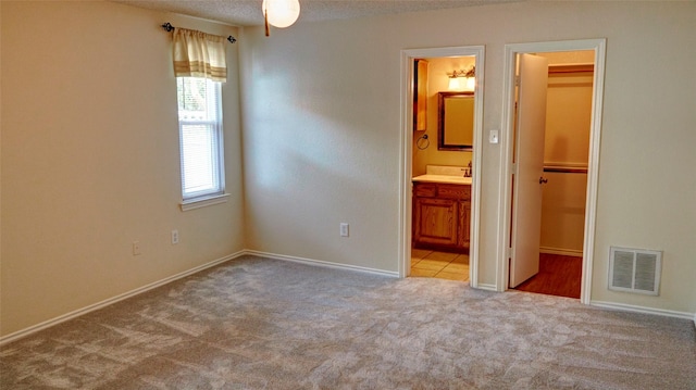 unfurnished bedroom with light carpet, a closet, ensuite bathroom, and a walk in closet