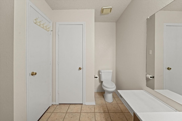 bathroom with toilet, tile patterned flooring, baseboards, and a textured ceiling