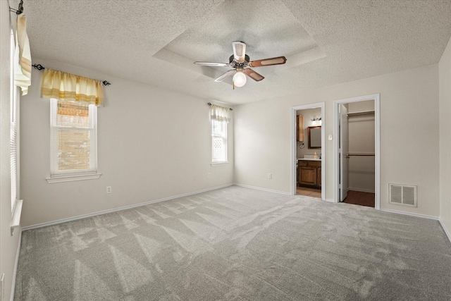 unfurnished bedroom with a textured ceiling, visible vents, a tray ceiling, carpet, and a walk in closet