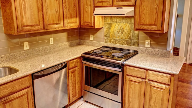 kitchen featuring ventilation hood, stainless steel appliances, tasteful backsplash, and light stone countertops