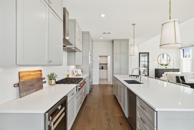 kitchen with stainless steel gas cooktop, wine cooler, hanging light fixtures, wall chimney range hood, and sink