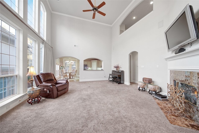 carpeted living room with ceiling fan, a high ceiling, crown molding, and a tiled fireplace