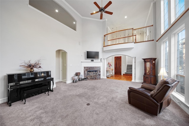 carpeted living room featuring ceiling fan, crown molding, and a towering ceiling