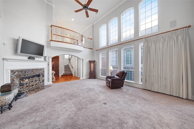 living room featuring ceiling fan, a fireplace, a towering ceiling, carpet flooring, and crown molding