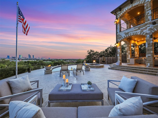 patio terrace at dusk with a city view, an outdoor living space with a fire pit, a balcony, and fence