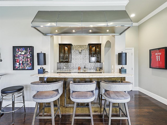 kitchen featuring backsplash, dark hardwood / wood-style floors, ventilation hood, ornamental molding, and a breakfast bar