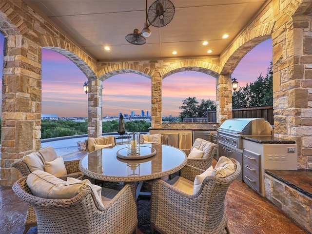 patio terrace at dusk with an outdoor kitchen, outdoor dining area, and grilling area