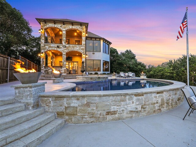 patio terrace at dusk featuring a pool with hot tub