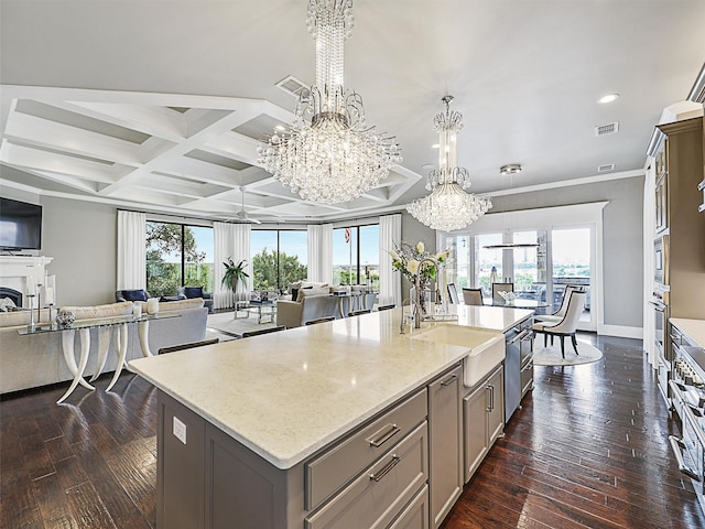 kitchen featuring coffered ceiling, a healthy amount of sunlight, a kitchen island with sink, beam ceiling, and sink