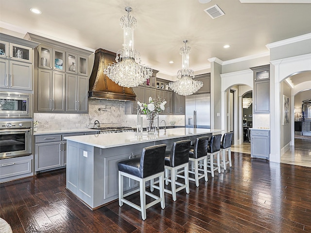 kitchen with a spacious island, pendant lighting, built in appliances, decorative backsplash, and premium range hood