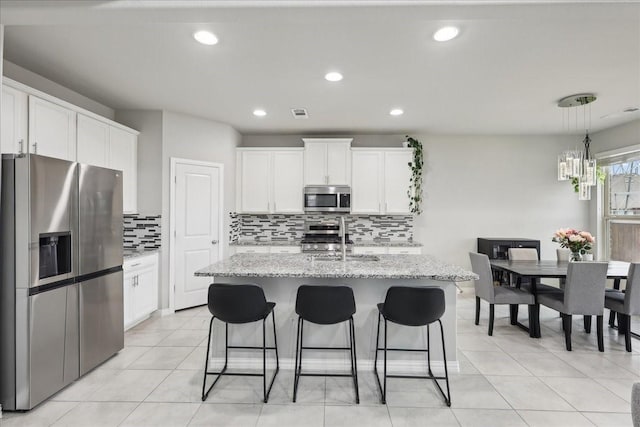 kitchen featuring white cabinetry, tasteful backsplash, an island with sink, stainless steel appliances, and light stone countertops