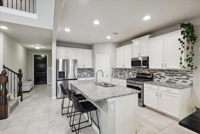 kitchen featuring sink, a kitchen island with sink, stainless steel appliances, light stone countertops, and white cabinets