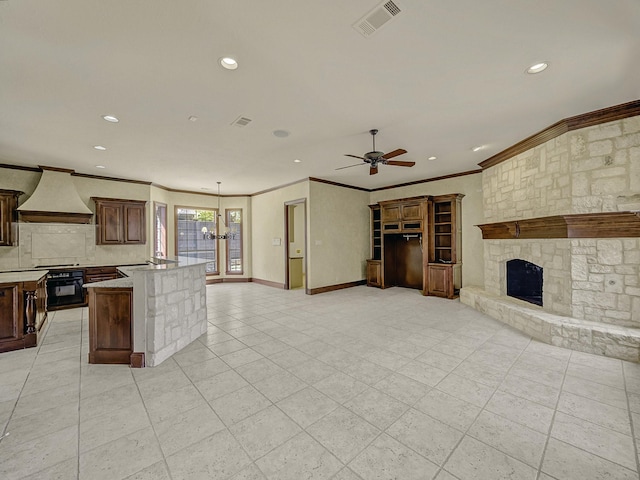 kitchen featuring stainless steel gas stovetop, custom exhaust hood, a stone fireplace, ornamental molding, and black oven