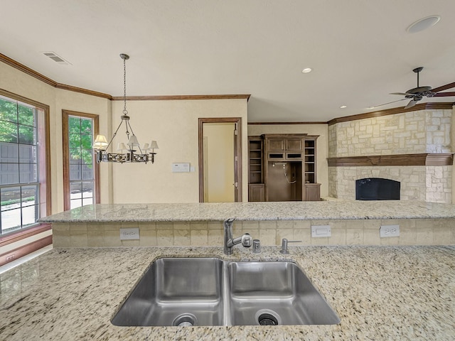 kitchen with crown molding, light stone counters, hanging light fixtures, and sink