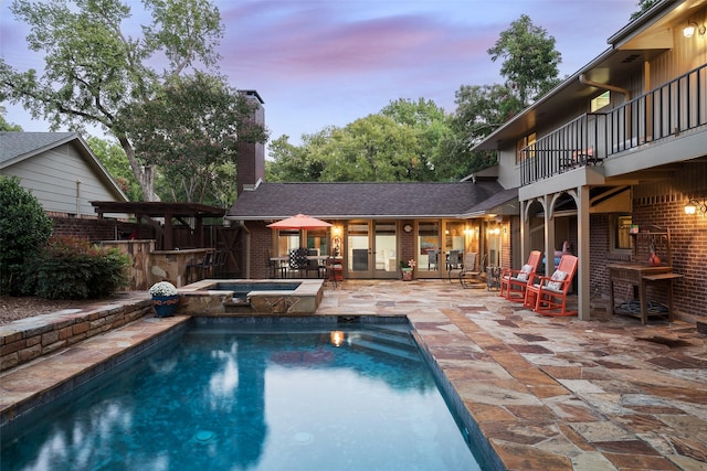 pool at dusk with an in ground hot tub, an outdoor bar, and a patio area