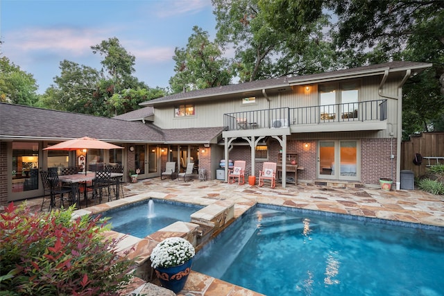 back house at dusk with a pool with hot tub, pool water feature, a patio area, and a balcony