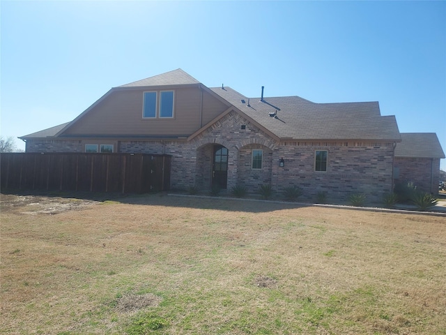 view of front of home with a front yard, brick siding, and roof with shingles