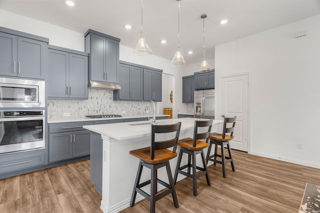 kitchen featuring appliances with stainless steel finishes, decorative backsplash, sink, hanging light fixtures, and a center island with sink