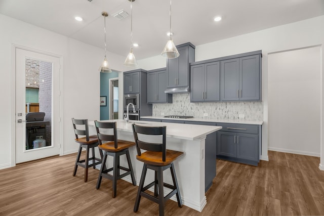 kitchen with decorative backsplash, hanging light fixtures, a kitchen island with sink, appliances with stainless steel finishes, and a kitchen breakfast bar