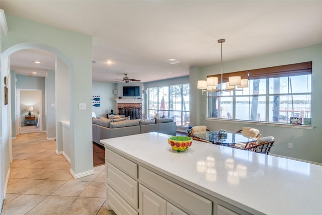 kitchen featuring white cabinetry, a brick fireplace, ceiling fan, light tile patterned flooring, and hanging light fixtures