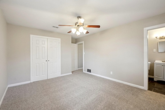 unfurnished bedroom with a closet, ceiling fan, connected bathroom, and dark colored carpet