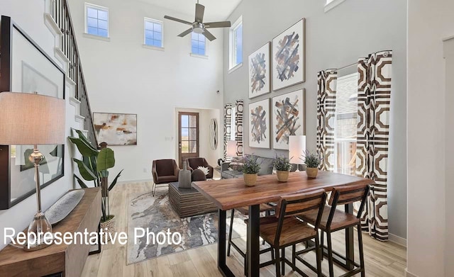 dining area featuring ceiling fan, a towering ceiling, and light hardwood / wood-style flooring