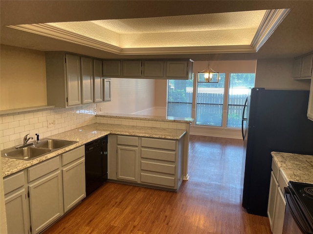 kitchen featuring dark hardwood / wood-style floors, black appliances, kitchen peninsula, sink, and a tray ceiling