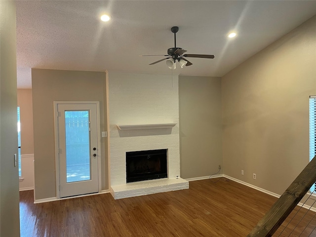 unfurnished living room featuring a textured ceiling, a brick fireplace, dark hardwood / wood-style floors, and ceiling fan