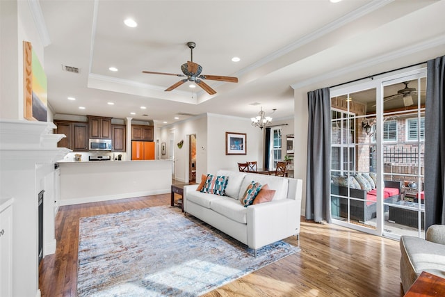 living room with a raised ceiling, ceiling fan with notable chandelier, and hardwood / wood-style floors