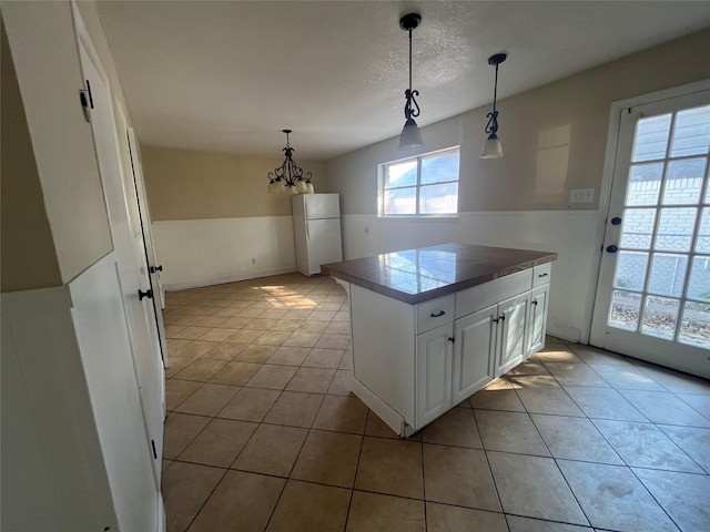 kitchen with a textured ceiling, decorative light fixtures, white cabinetry, white fridge, and light tile patterned floors