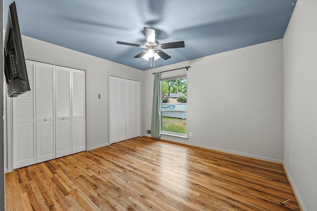 unfurnished bedroom featuring ceiling fan, light hardwood / wood-style flooring, and two closets