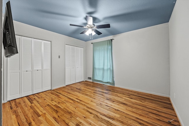 unfurnished bedroom with ceiling fan, light wood-type flooring, and two closets